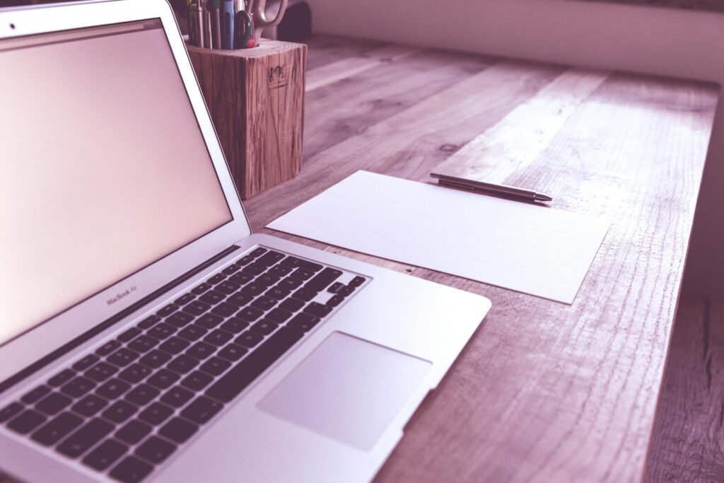 A clean and organized desk with a laptop, paper, and pen, ideal for productivity.